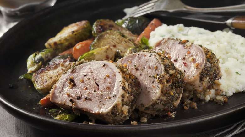 spice-crusted pork tenderloin, cooked to a perfect medium-rare, served on a black plate with herbed mashed potatoes and roasted vegetables