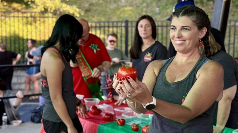woman holding up a red tomato at a contest during the pittston tomato festival