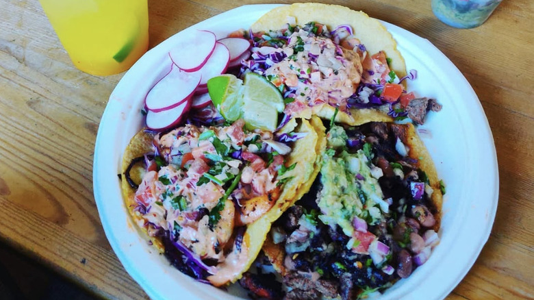 Three tacos on a white plate on a wooden table