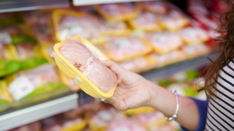 hand holding packet of raw chicken in grocery store
