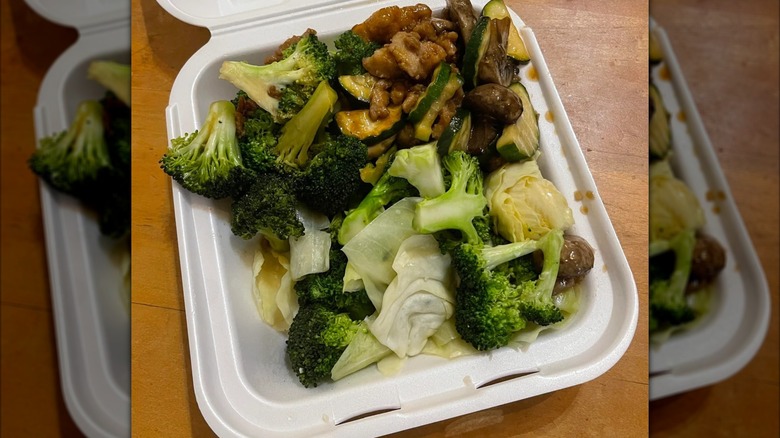 Takeout container with greens and chicken and sauce, mirrored image