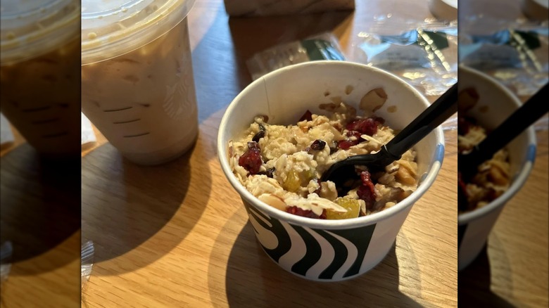 Oatmeal with fruit in Starbucks pot with spoon next to takeout coffee, mirrored image