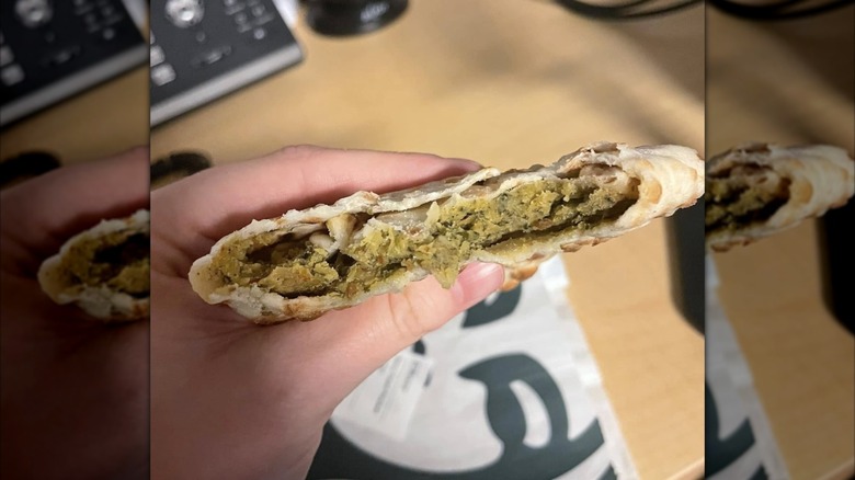 close up of hand holding spicy falafel pocket in front of desk, mirrored image