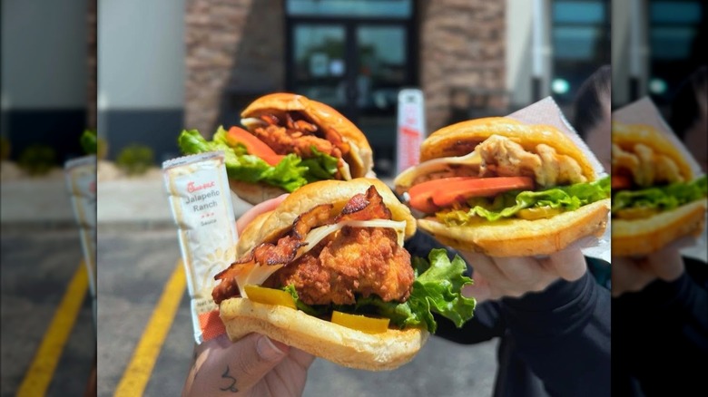 Hands holding up Chick-fil-A Jalapeño Ranch Club sandwiches with parking lot backdrop