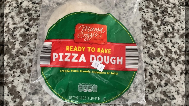 Packet of Mama Cozzi's Pizza Kitchen Ready to Bake Pizza Dough on granite kitchen counter, mirrored border