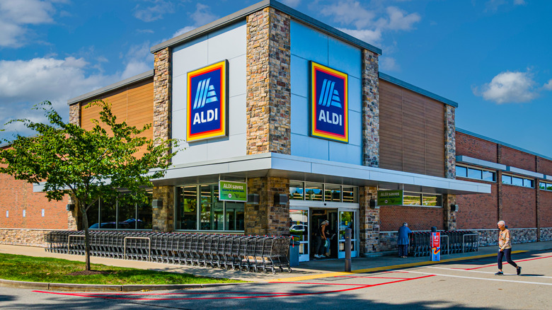 A customer approaches the front entrance of an Aldi Grocery store in front of blue sky