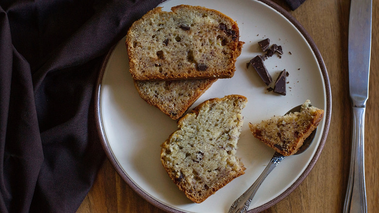 Plate with slices of eggless banana bread and chocolate, next to knife and table cloth