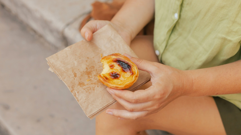 Woman sat on a step holding egg tart pastry called Pastel de Nata