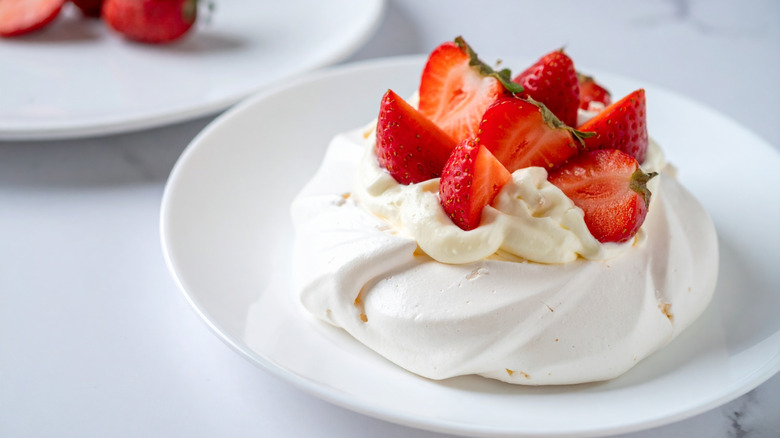 Pavlova dessert with whipped cream and fresh strawberries served on white plate