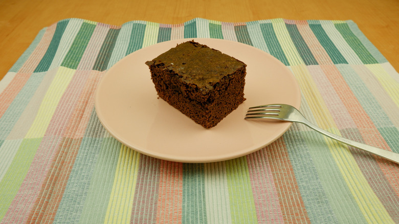 Slice of chocolate wacky cake with fork on patterned table mat
