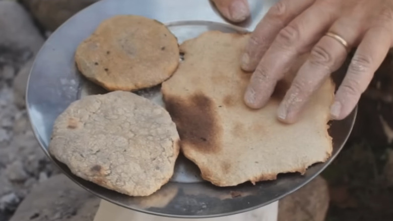 close up of hand touching ash cakes on a silver plate