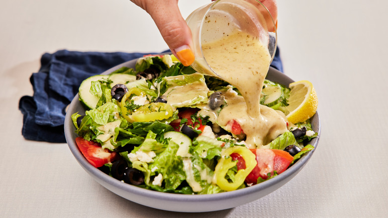 woman's hand pouring dressing over a salad