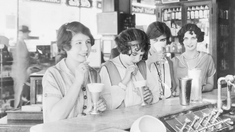 Flappers at a soda fountain drinking milk shakes in 1926, black and white image