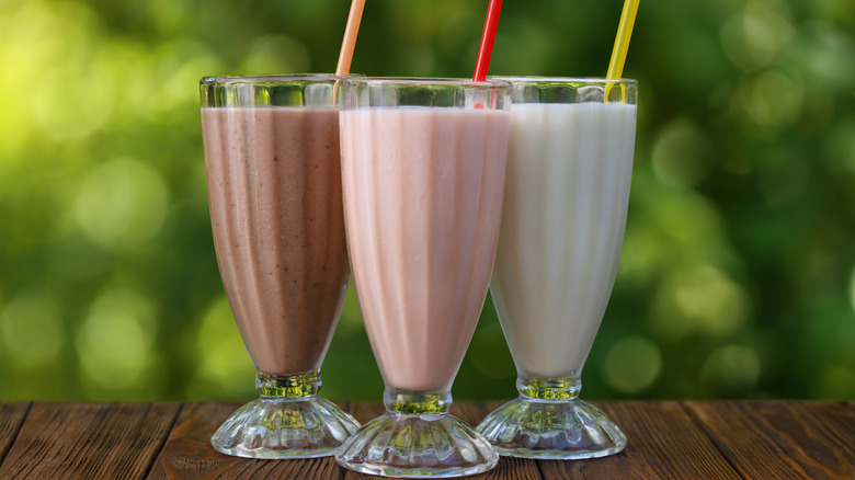 set of three milkshakes with straws on table outside