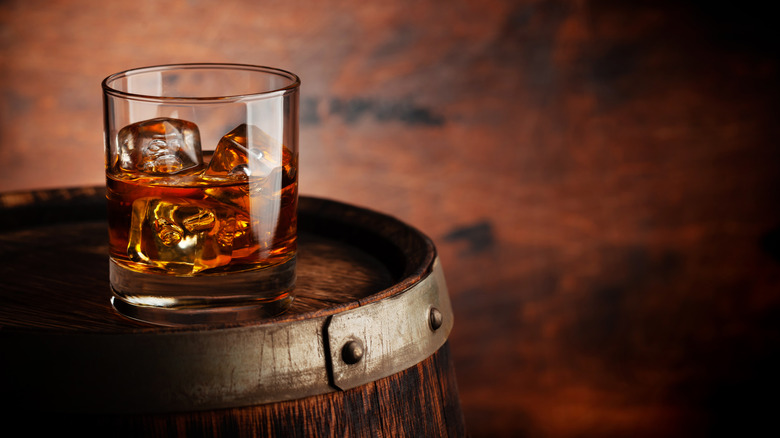 A glass of whiskey with ice cubes on a wooden barrel