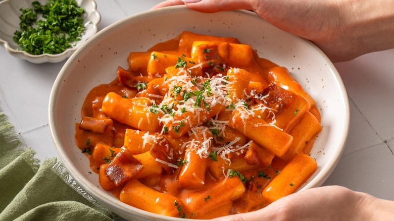 A lady placing a bowl of bibigo spicy carbonara tteokbokki on a countertop with cilantro on the side