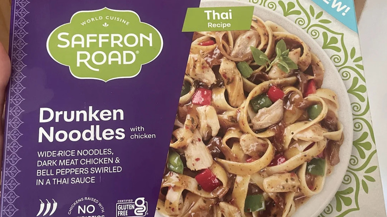 A consumer showing a box of Saffron Road drunken noodles with chicken frozen meal box
