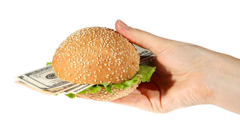 Hand holding sandwich with lettuce and dollar bills inside