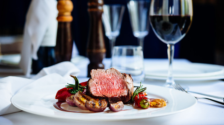 An upscale steak dinner on table with wine and tableware
