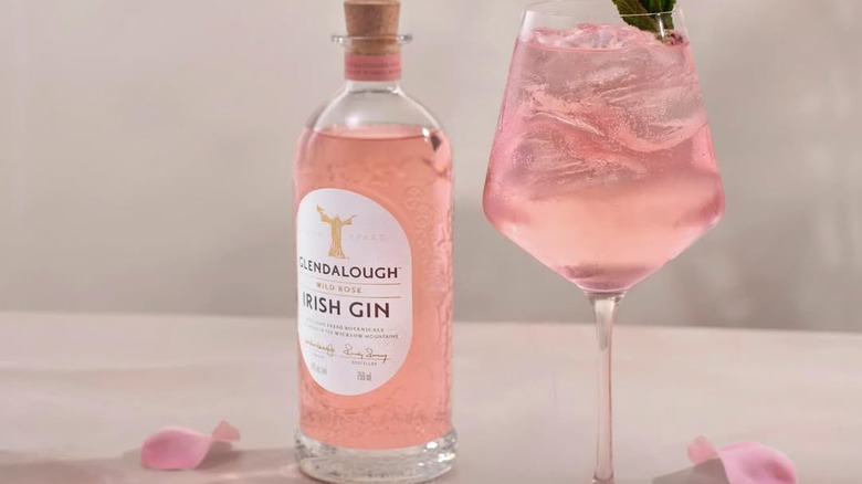 A bottle of Glendalough Rose Gin on a table next to a large filled glass and rose petals