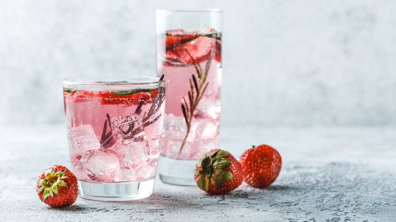 Two glasses of pink gin and ice that also contain strawberries and rosemary