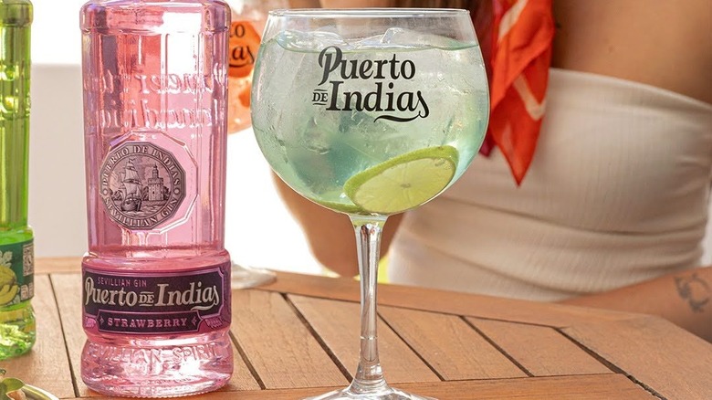 A bottle of Puerto de Indias Strawberry Gin on a table next to a large filled glass