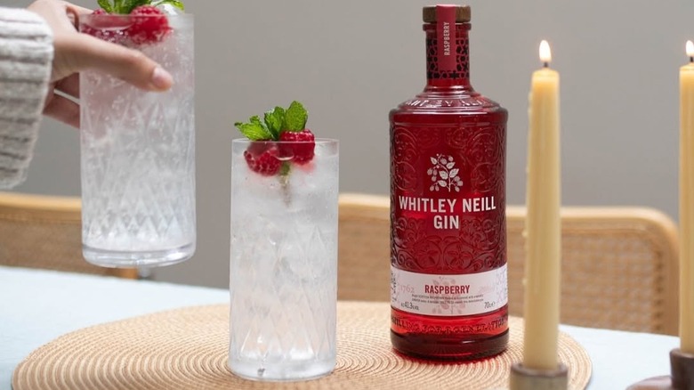 A bottle of Whitley Neill Raspberry Gin on a table next to lit candles and filled glasses