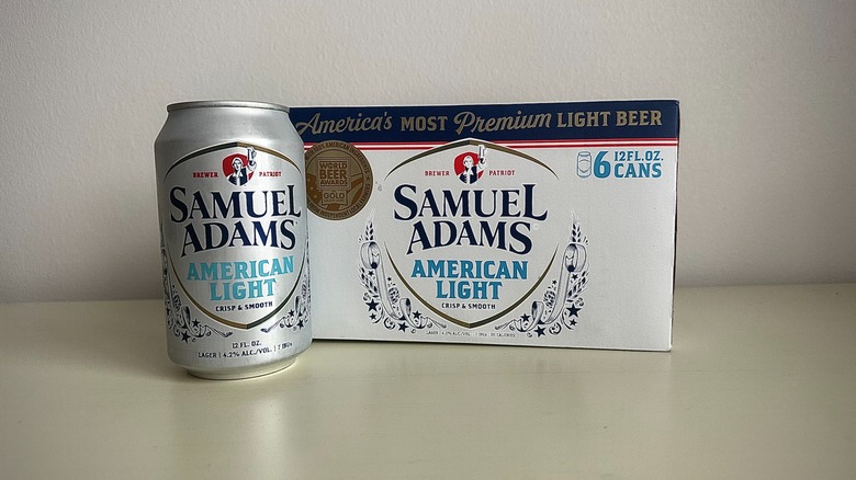 The front of a can of Samuel Adams American Light, next to the box of a six pack