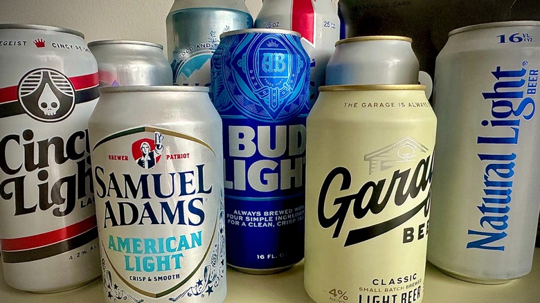 The front of nine seperate cans of light beers produced by different breweries, including Cincy Light, Samuel Adams American Light, Coors Light, Busch Light, Bud Light, Garage Beer, Miller Lite, and Natural Light