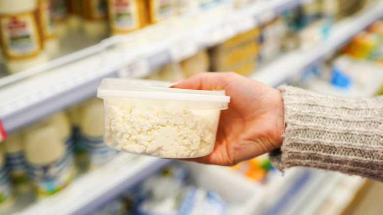 Hand holding tub of cottage cheese in grocery store