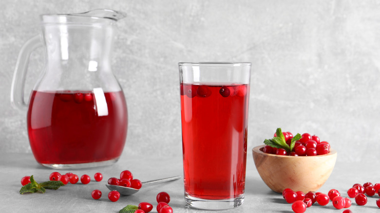 Cranberry juice in glass and pitcher surrounded by cranberries