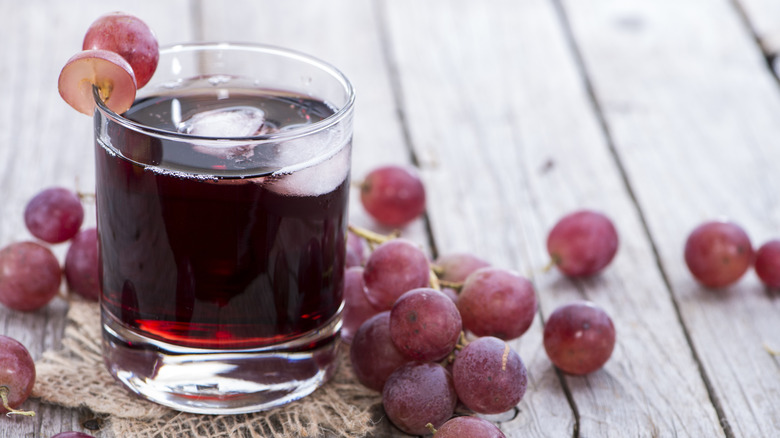 Grape juice in glass surrounded by grapes on table