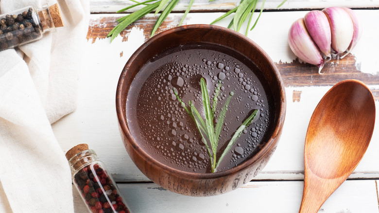 Beef broth in wooden bowl with herbs and spices