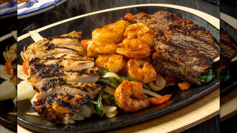 Beef, chicken, and shrimp on plate with peppers and onions