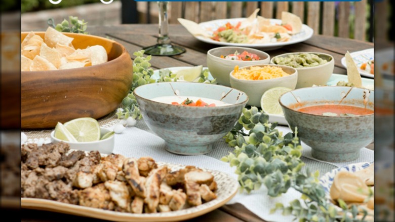 Table set with platters and bowls of fajita meat, chips, salsas, and toppings