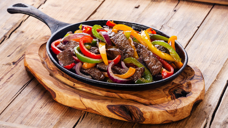 Skillet of steak fajitas on wooden board