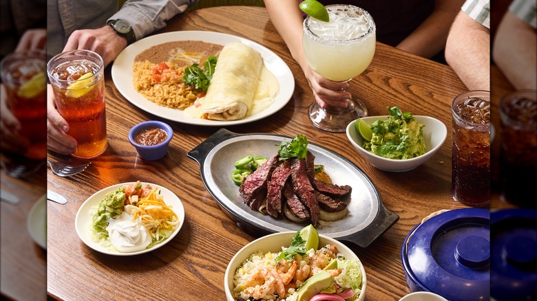 Table with assortment of plates and dishes including steak fajitas, guacamole, and cocktails