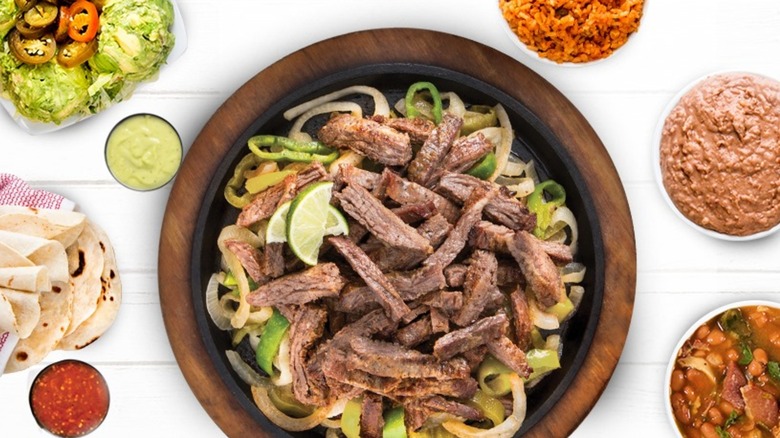 Plate of fajita steak on peppers and onions with assorted bowls on sides