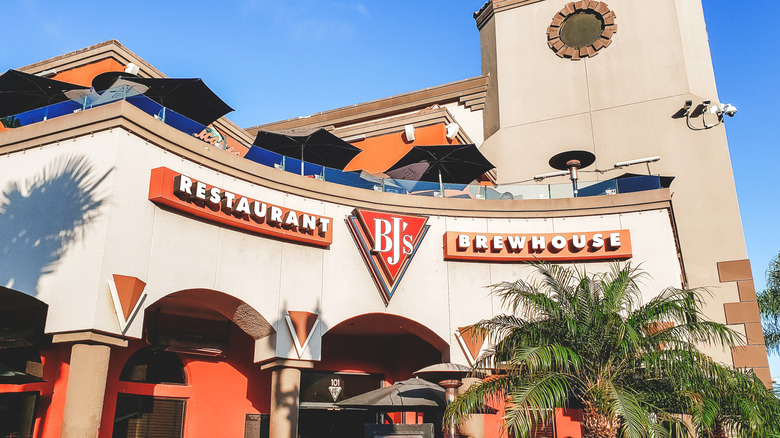 Curved facade of a BJ's Restaurant & Brewhouse behind a palm tree