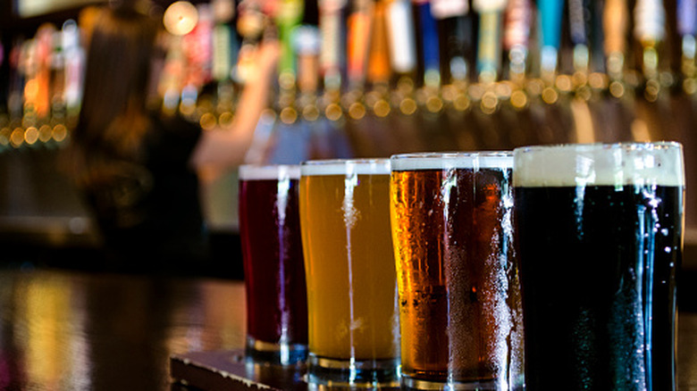 Flight of beers in the foreground as a bartender draws another glass from a large selection of taps
