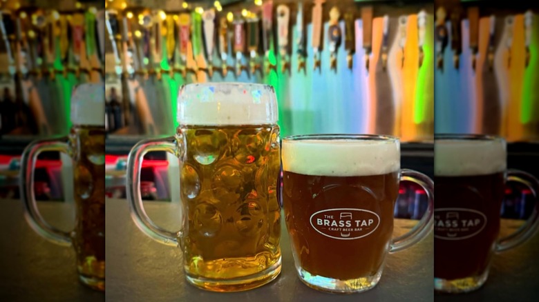 Two sizes of beer resting on a The Brass Tap bar in front of taps
