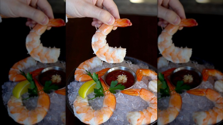Person holding a piece of jumbo shrimp over ice bowls with sauce and shrimps