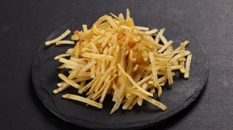 A large pile of potato sticks on a dark round stone.