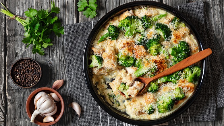 Chicken Divan in round deep dish with spoon on wood table.