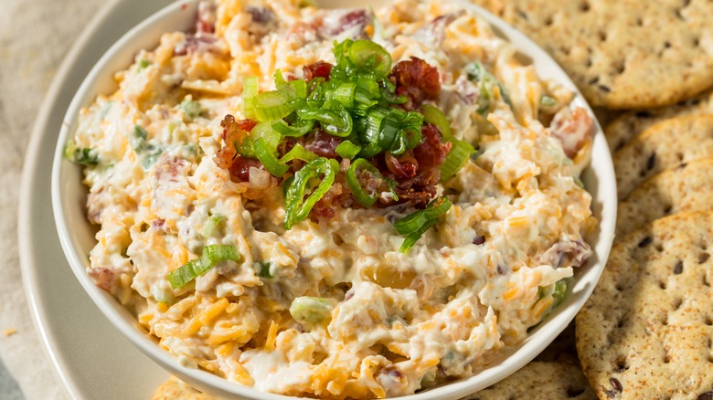 Million dollar dip in small white bowl with a side of crackers.