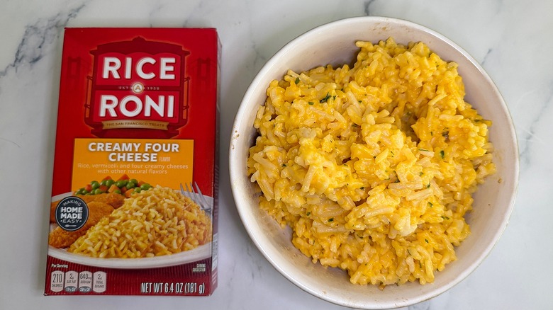 Top-down shot of bowl of Creamy Four Cheese Rice-A-Roni next to box on marble surface