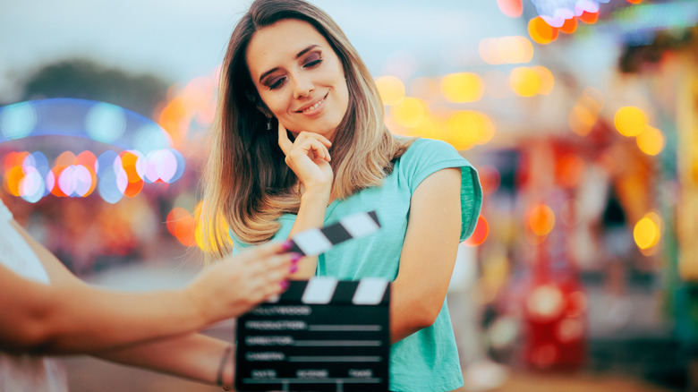 woman posing in front of clapper board against blurred lit up background