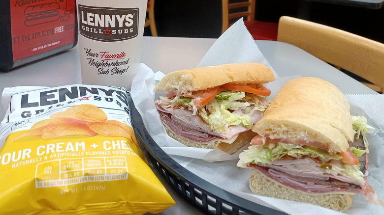 A sub sitting in a basket next to Lenny's chips and a Lenny's take-out cup