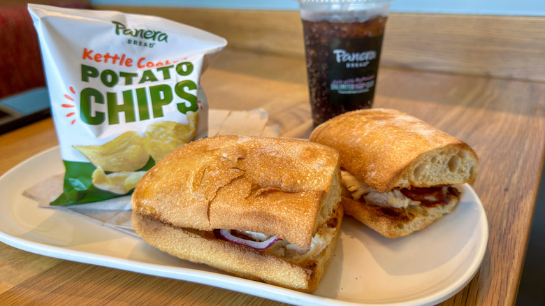 A Panera sandwich, chips and soda sitting on a counter