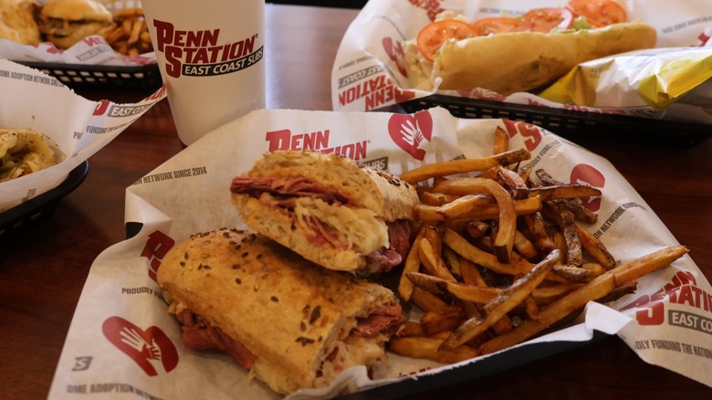 A Penn Station sub with dries and a drink surrounded by other meals